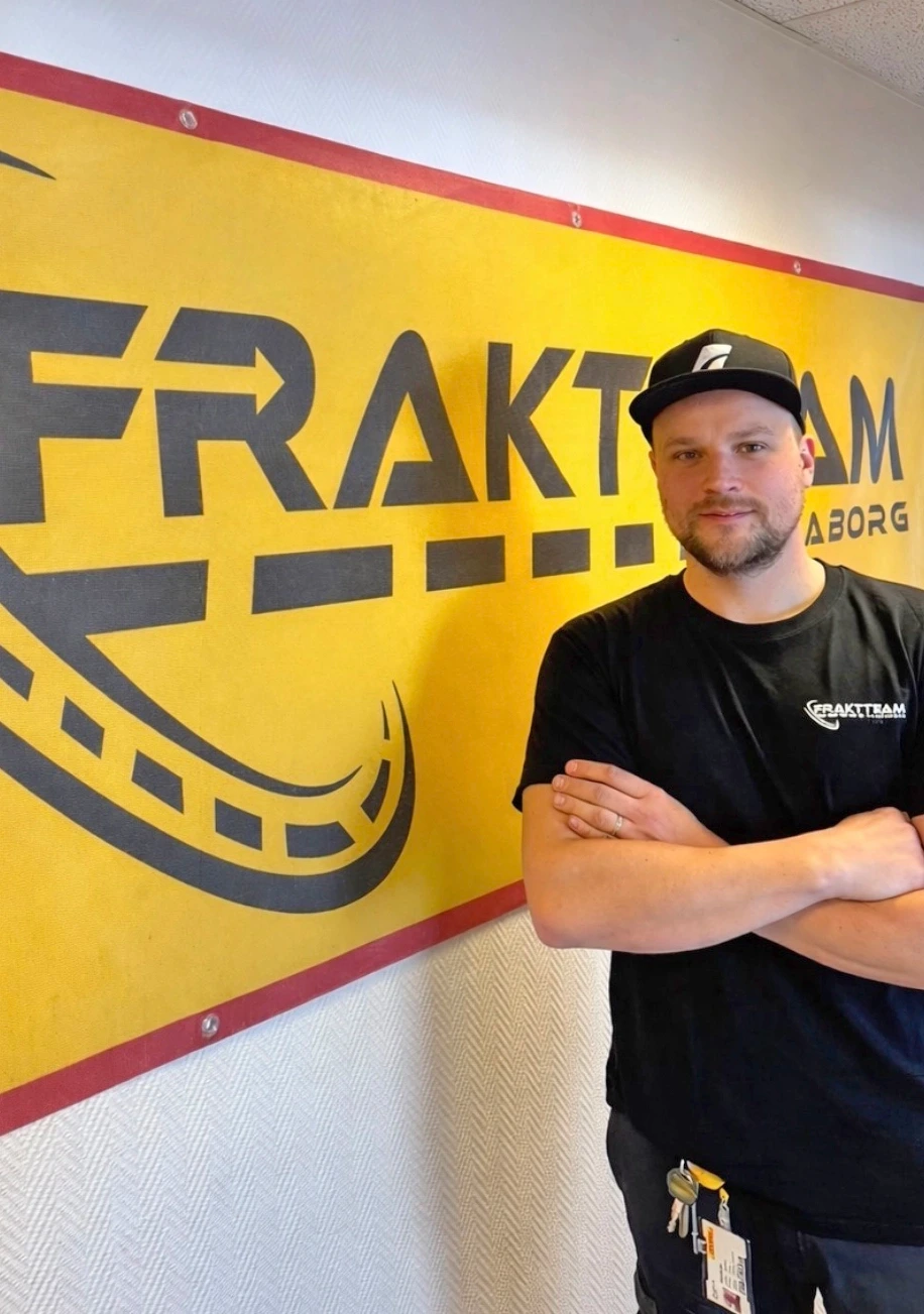 Tobias står i t-shirt och keps framför en skylt med företagets logo